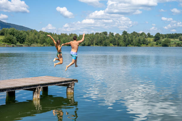 pareja joven saltar en lake - swimming trunks bikini swimwear red fotografías e imágenes de stock