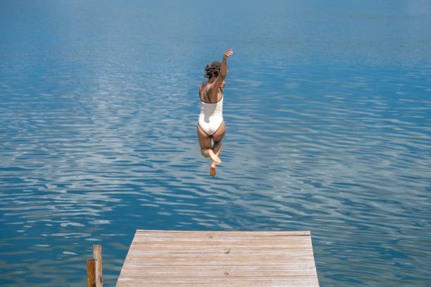 Woman jumping into the water of volcanic lake surrounded by forest in Banlung, Cambodia, travel destination. Toned vintage style