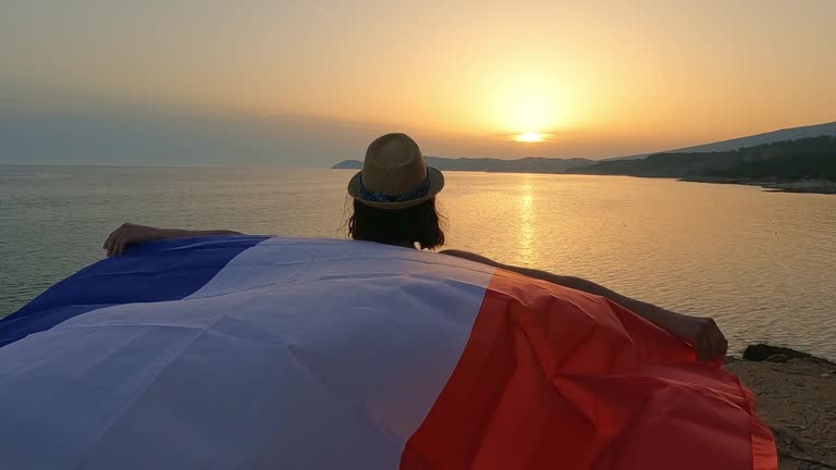 Young Caucasian woman waving a French flag on the seaside during sunset