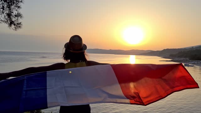 Young Caucasian woman waving a French flag on the seaside during sunset