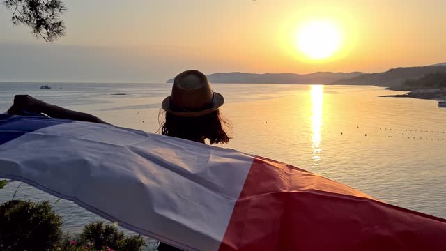 Young Caucasian woman waving a French flag on the seaside during sunset