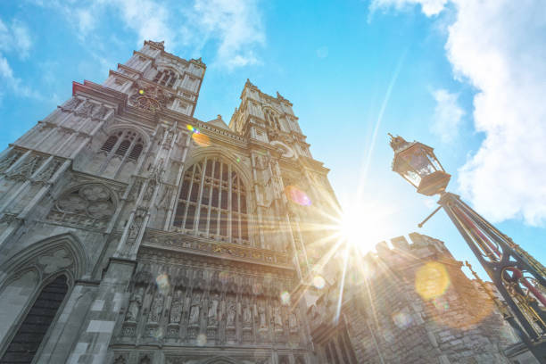 In this photo, we see the magnificent facade of Westminster Abbey towering above us, captured from a low angle view. The grandeur of the historic building is accentuated by the warm, golden light of the peeking sun on a beautiful summer day. The image captures the essence of the Abbey's timeless beauty and the awe-inspiring feeling one gets standing in its presence. It is a stunning snapshot of one of London's most iconic landmarks, bathed in the glow of a perfect summer day.