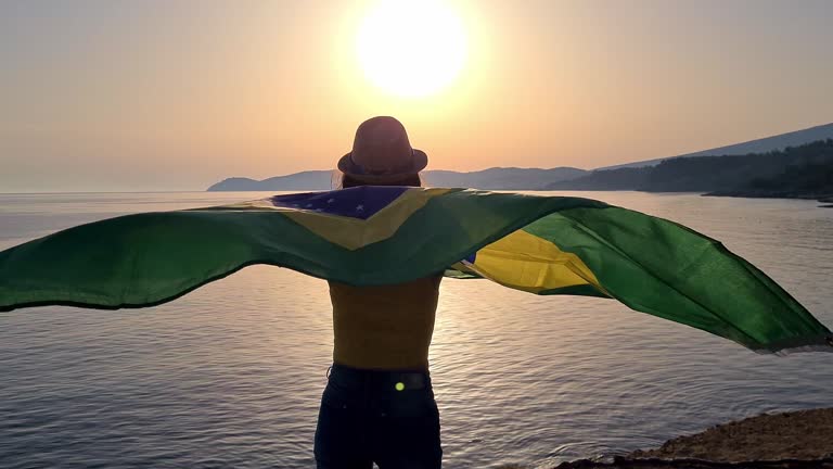 Young Caucasian woman waving a Brazilian flag on the seaside during sunset