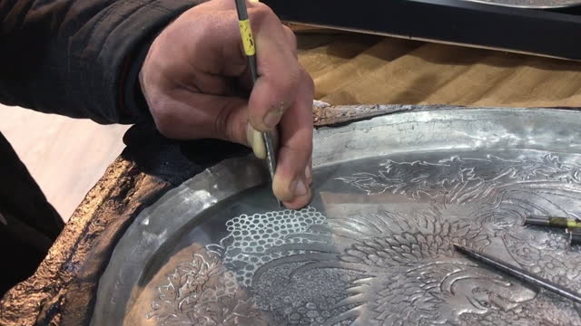 Artisan hands gouging tin plate with nail and hammer