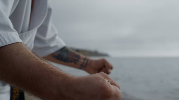 Muscular man fist training karate punches on cloudy beach close up. Unrecognizable athlete practicing martial arts on sandy seacoast summer morning. Strong fighter hands doing exercises wearing kimono