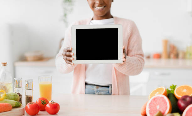 istock Cheerful millennial black female shows tablet with empty screen at kitchen interior near table with organic fruits 1468483138
