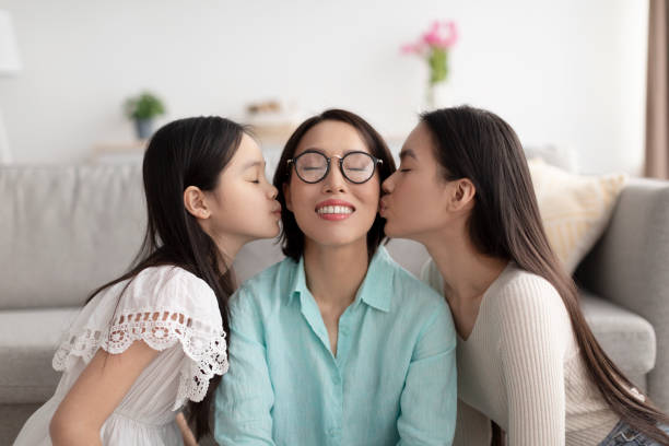 家で大人の娘と小さな孫娘にキスされる幸せな成熟したアジア人女性 - grandmother granddaughter senior adult teenager ストックフォトと画像