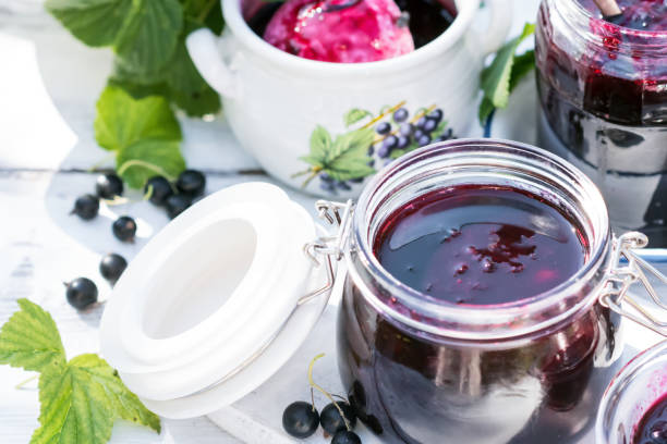 istock Cooked homemade black currant jam in jar on white wooden table background, fresh black currant jam close up 1468484989