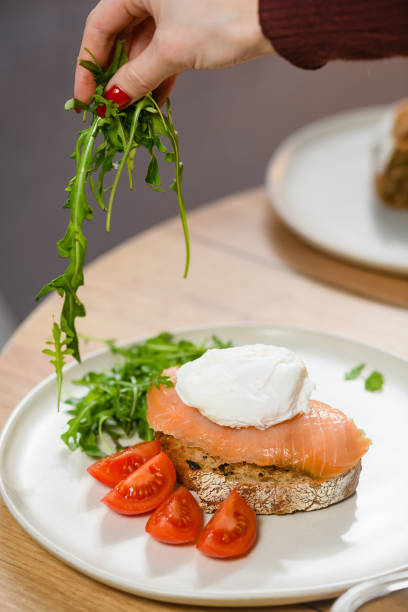 A girl puts arugula on a dish with a sandwich and a poached egg A girl puts arugula on a dish with a sandwich and a poached egg. Breakfast concept. egg cherry tomato rye stock pictures, royalty-free photos & images
