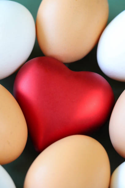 istock Full frame image of a model red heart surrounded by mixed coloured chicken eggs, white and brown shells, studio shot, green background, elevated view, healthy eating concept 1468486398