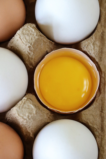 Stock photo showing close-up, elevated view of a half a dozen mixed white and brown coloured eggs in open disposable cardboard egg box.