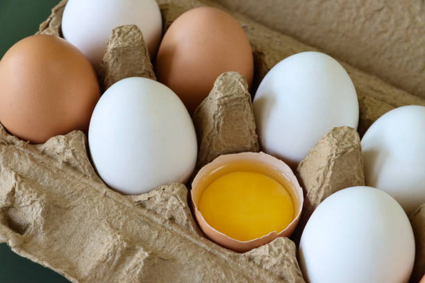 istock Close-up image of eight mixed coloured chicken eggs, five white and three brown shells, one broken egg with view of yolk and albumen, green background, elevated view, focus on foreground 1468486672