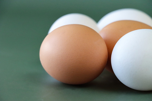 Stock photo showing close-up view of batch of mixed white and brown coloured eggs on a green background.