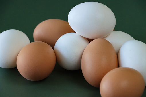 Stock photo showing close-up view of stack of mixed white and brown coloured eggs on a green background.