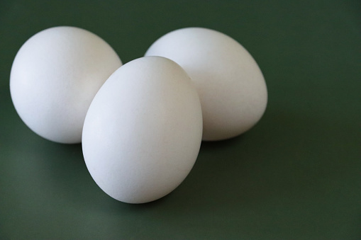 Stock photo showing close-up view of batch of white coloured eggs on a green background.