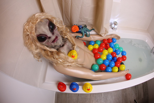 A very spooky alien is relaxing in the bathtub. He has a fit torso and lays down in the water.