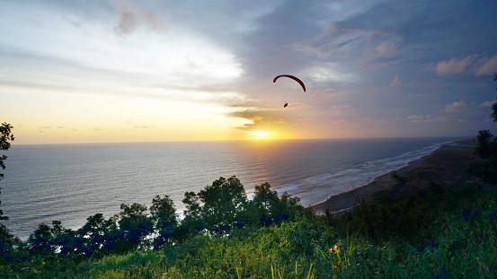 picture of skydiving with a parachute over the sea at sunset in the evening in parangtritis beach yogyakarta, indonesia.
