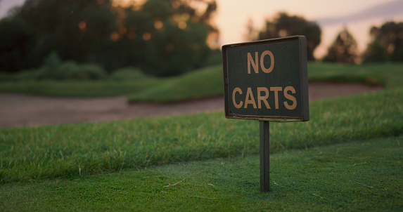 Golf course grass sign in empty grass fairway. Transport restriction in sunset field evening. Peaceful golfing landscape view outdoors. Serene nature on sport fairway. Beautiful no people concept.