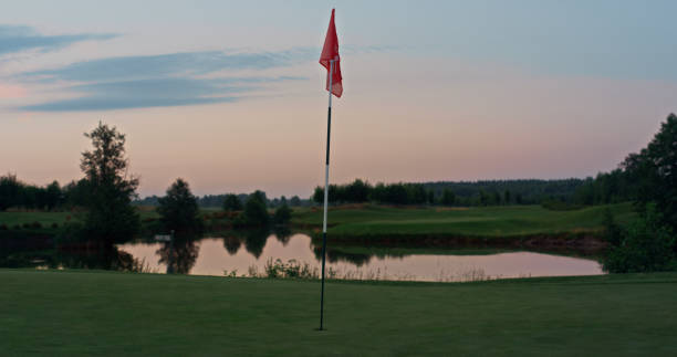 istock Golf course red flag in golfing hole. Flagstaff on empty green course sunset. 1468489057