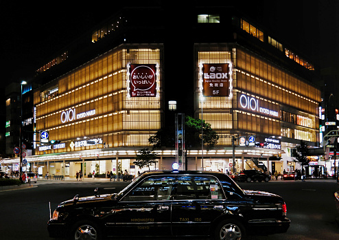 Kyoto, Japan - Sept, 2017: Kyoto Oioi Marui department store and black vintage taxi cab with night lights. Marui is a Japanese retail company which operates a chain of department stores