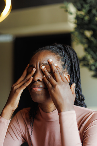 Young unhappy afro american woman with dreadlocks crying covering eyes with hands in coffee house closeup. Depressed black girl suffering, despaired, upset. Tiredness, unfair, troubles.