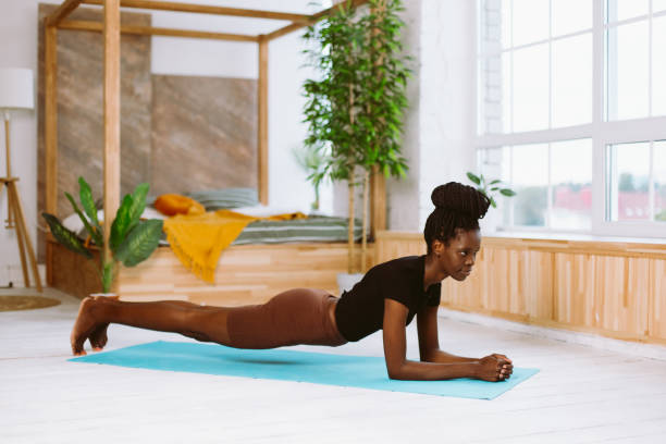 istock Athletic afro american woman with dreadlocks standing in elbow plank side view, training on gymnastic mat in decorated studio. Muscle strengthening, pumping up, fitness, keeping body fit 1468495538