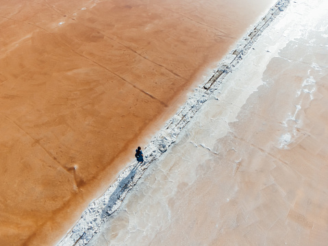 Aerial view of a woman walking in the middle of orange salt flats in Sicily, Italy. Trapani salt flats.