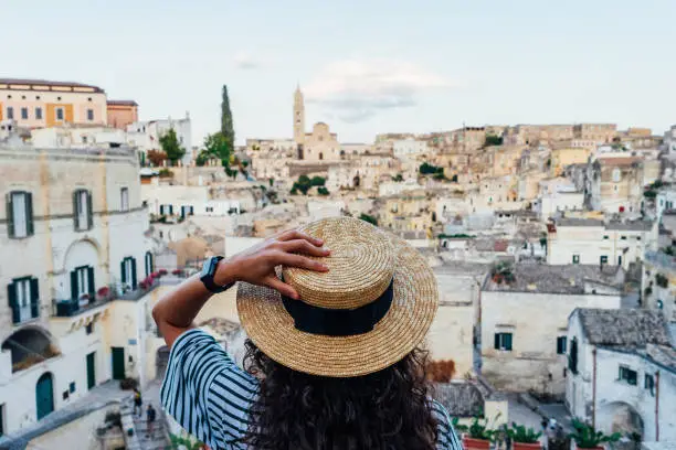 A woman with a straw hat is admiring the beautiful Matera ancient city. Sassi di Matera, a famous international landmark in Southern Italy.