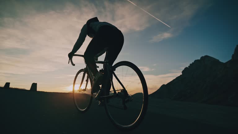 Cyclist riding bicycle uphill on road in sunrise mountains