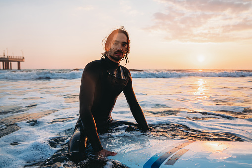 Portrait of a man sitting on his surfboard in the sea. He's wearing a wetsuit.