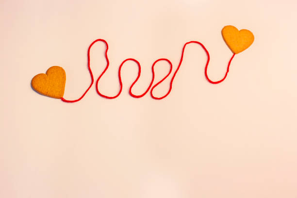 two hearts connected by red thread on soft pink background isolated copy space