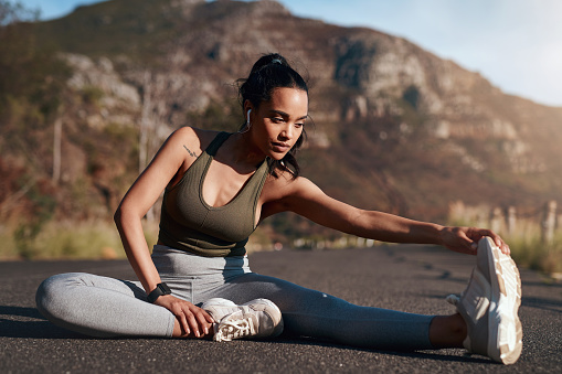 Exercise, running and stretching with a sports woman outdoor on a road in the mountain for cardio or endurance. Fitness, workout and warm up with a female runner getting ready for a run in nature