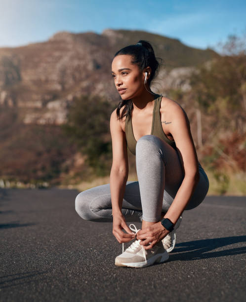 Shoes, road and runner woman getting ready for training, exercise or mountain running in sports sneakers and fashion. Young athlete or person tying her laces with cardio, fitness or workout music stock photo