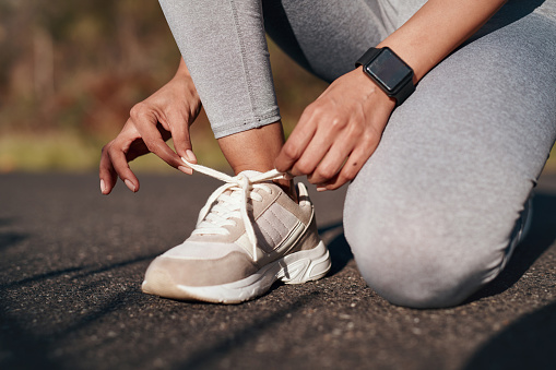 Sports, street and athlete tie her shoes before training for a running marathon, race or competition. Fitness, workout and woman preparing for an outdoor cardio exercise for health in the road.