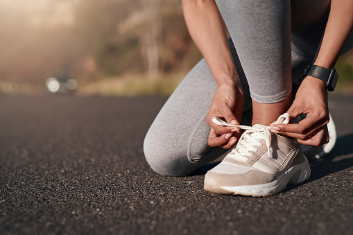 Fitness, road and woman tie her sneakers before training for a running marathon, race or competition. Sports, workout and female athlete preparing for outdoor cardio exercise for health in the street