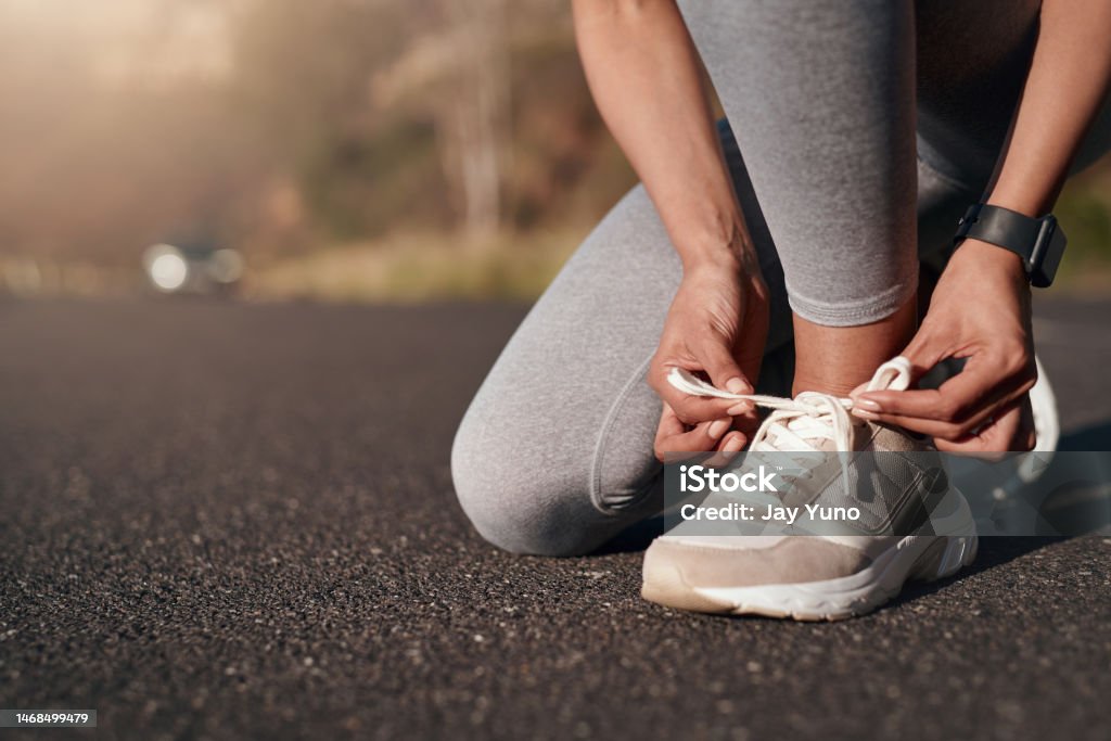 Fitness, road and woman tie her sneakers before training for a running marathon, race or competition. Sports, workout and female athlete ready to start an outdoor cardio exercise for health in street Fitness, road and woman tie her sneakers before training for a running marathon, race or competition. Sports, workout and female athlete preparing for outdoor cardio exercise for health in the street Sports Shoe Stock Photo