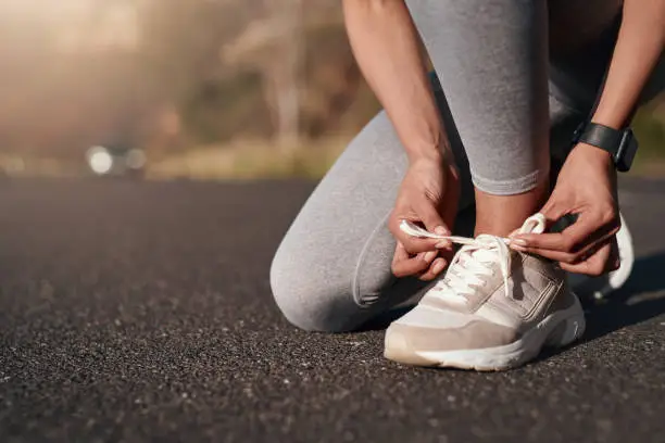 Photo of Fitness, road and woman tie her sneakers before training for a running marathon, race or competition. Sports, workout and female athlete ready to start an outdoor cardio exercise for health in street