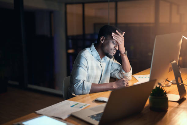 Burnout, night or black man with headache in office for computer 404 glitch, coding anxiety or mental health. Sad, tired or developer on tech for programming depression, work stress or software fail stock photo