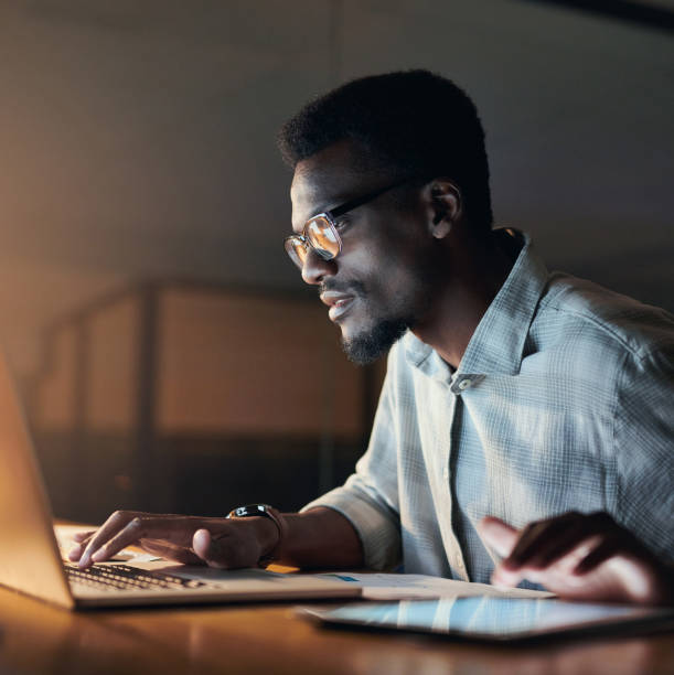 Businessman, thinking or laptop typing in night office on financial management, insurance budget or company investment. Black man, employee or working late on technology, finance growth or idea goals stock photo