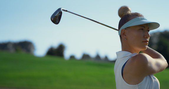 Confident woman playing golf on fairway. Golfer swinging hitting ball at summer country club. Close up sporty golfing player training at green course. Blonde girl spend time outdoors. Active concept.