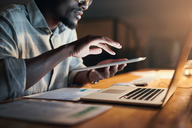 Black man, hands and tablet in night office for financial management, insurance budget or interactive data analytics. Zoom, businessman and working late on technology for finance growth or investment stock photo