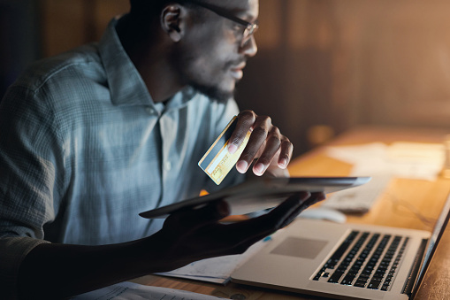 Businessman hands, tablet or credit card in night office for financial management, internet payment or laptop investment. Black man, thinking or working late on technology budget in finance planning