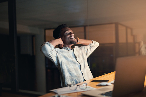 Relax, night and black man in the office on a break taking a nap after working on a project with a deadline. Tired, rest and exhausted African male employee sleeping by his desk in the workplace.