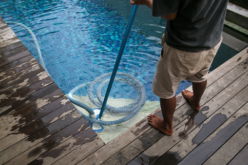 Man cleaning swimming pool with vacuum tube cleaner. Weekly pool maintenance. Pool cleaning service.