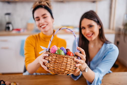 Portrait of two beautiful young women sitting at home and holding a basket with Easter Eggs for Easter.