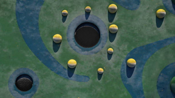 blue rubber surface of a playground with yellow scoops and colored spots in the frost of human footprints. raised lenses such as balls, wooden benches and circular trampolines sunk into the terrain. - school bench above bildbanksfoton och bilder