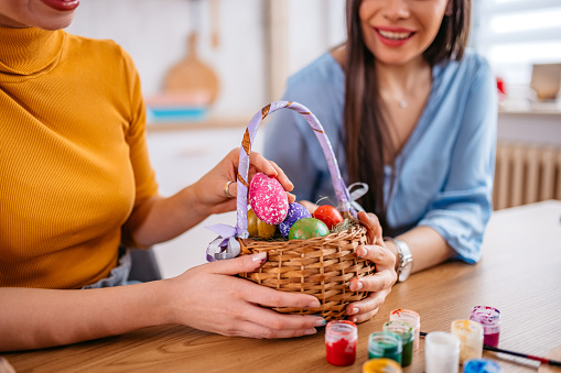 Two beautiful young women sitting at home and holding a basket with Easter Eggs for Easter.