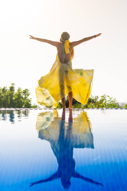 Model with yellow dress raising arms in an outdoor pool stock photo