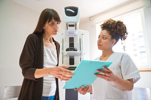 Woman analyzing medical results with nurse against mammogram in medical clinic.