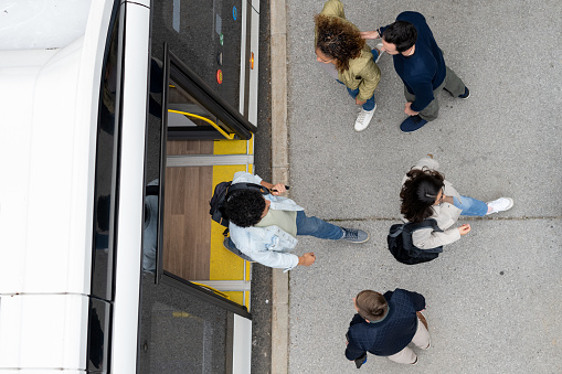 Overhead view of passengers exiting and boarding in bus at bus stop in city.